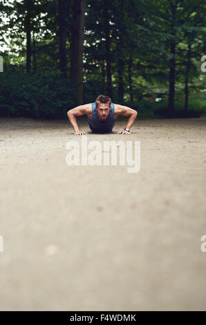 Niedrigen Winkel Ansicht eines Fit jungen Mannes Liegestütz in einem Park als Teil seiner täglichen Übung Regime mit Vordergrund Exemplar zu tun Stockfoto