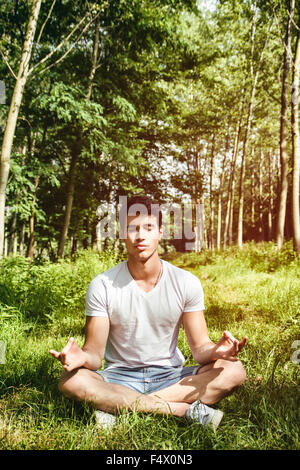 Hübscher junger Mann während der Meditation oder ein Outdoor-Yoga Übung Schneidersitz sitzen auf grasbewachsenen Boden allein im Wald Stockfoto