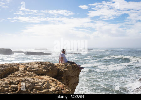 Mann sitzt auf dem Rand der Klippe an der kalifornischen Küste mit Blick auf den Ozean. Stockfoto