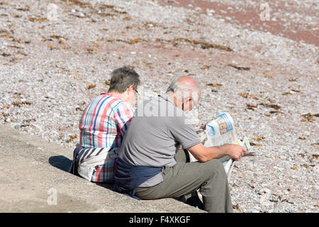 Älteres Ehepaar lesen Zeitung setzte auf Stufen am Oddicombe Strand an heißen September Tag in Torquay, Devon, England Stockfoto