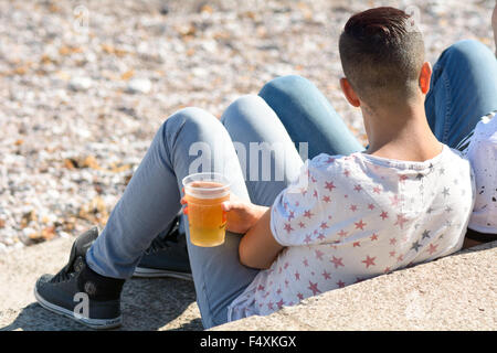 Zwei Männer sitzen auf den Stufen trinken Bier am Oddicombe Strand, Blick auf das Meer an heißen Tag in Torquay, Devon, England Stockfoto