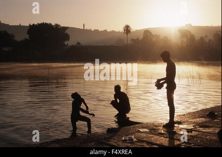 Drei junge Männer baden am frühen Morgen in einem Fluss. Im Hintergrund ist der Vijay stambh (Turm des Sieges) sichtbar. Stockfoto