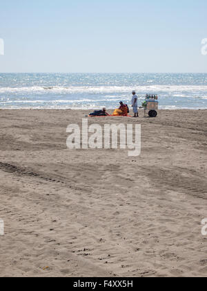 Zwei Hausierer mit einem Bauchladen bieten ihre waren an Touristen liegen am einsamen Strand von Lido di Ostia (Rom, Italien) Stockfoto