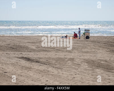 Zwei Hausierer mit einem Bauchladen bieten ihre waren an Touristen liegen am einsamen Strand von Lido di Ostia (Rom, Italien) Stockfoto