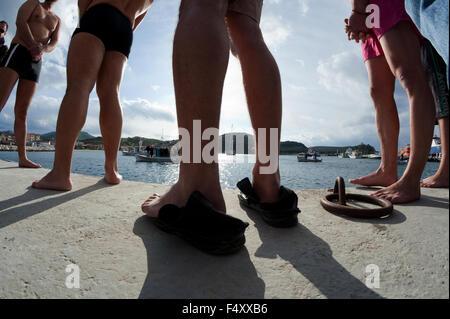 Silhouette Schwimmer Beine auf der Anklagebank vor dem Abwurf des Kreuzes in Myrina Stadthafen. Heilige drei Könige Feier Lemnos Griechenland Stockfoto