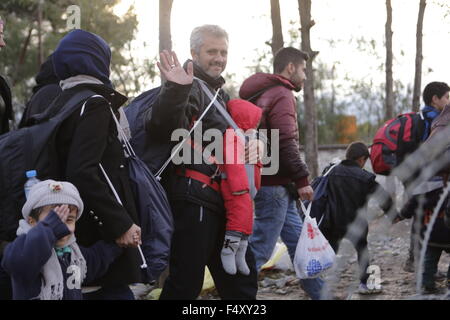 Idomeni, Griechenland. 23. Oktober 2015. Ein Flüchtling trägt sein Kind über die Grenze zu Mazedonien und Wellen in die Kamera. Tausende Flüchtlinge überqueren die Grenze zwischen Griechenland und Mazedonien täglich um die kleine griechische Stadt Idomeni, trotz der sich verschlechternde Wetter und starkem Regen. Hier nehmen sie einen kurzen Stopp für einige Vorräte und warten ihrerseits auf die Grenze zu überqueren. Bildnachweis: Michael Debets/Pacific Press/Alamy Live-Nachrichten Stockfoto