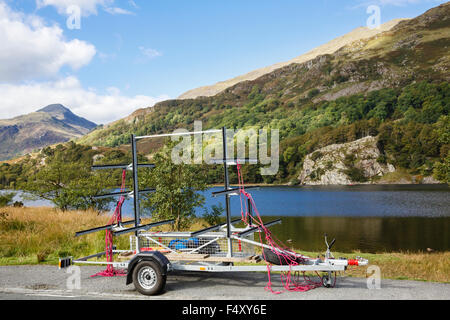 Leere Kanu Anhänger am Straßenrand mit Menschen Kanufahren auf Llyn Gwynant See in Snowdonia-Nationalpark. Nantgwynant, Wales, UK Stockfoto