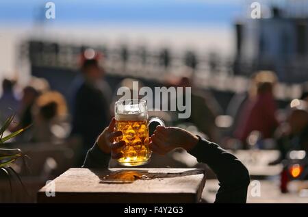 Stegen, Deutschland. 24. Oktober 2015. Ein Mann reicht für ein Bier auf dem Tisch über seinem Kopf in einem Biergarten am Ammersee in der Nähe von Stegen, Deutschland, 24. Oktober 2015. Foto: KARL-JOSEF HILDENBRAND/Dpa/Alamy Live News Stockfoto