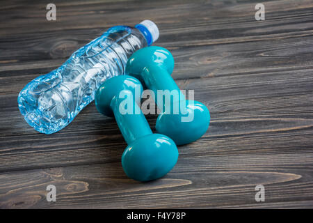 Zwei blaue Hanteln und eine Flasche Wasser auf hölzernen Hintergrund Stockfoto