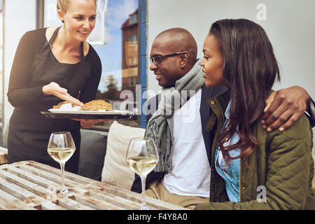 Lächelnd Kellnerin mit afroamerikanischen Liebespaar ihre Küche wie sie Arm in Arm auf einen Tisch im Restaurant zu sitzen Stockfoto