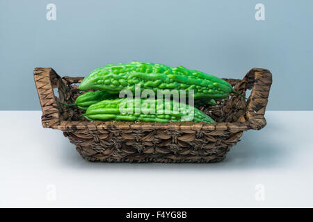 Ganze Karela bittere Melone Caraili Studio schließen auf blauem Hintergrund in Stroh Korb Stockfoto