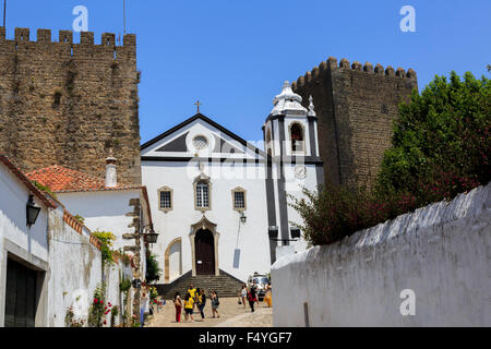 Touristische vor der Igreja de Santiago (Kirche von Santiago), die auf beiden Seiten von den alten Mauern in Obidos, Portugal eingerahmt ist Stockfoto