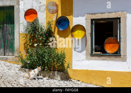 Dekorative Gerichte hängen auf der Außenseite eine bunt bemalte Hauskatze sitzt tränken Sie die Sonne in Obidos, Portugal Stockfoto