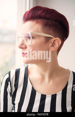 rothaarige Frau mit schwarzer Brille Blick durch Fenster Stockfoto