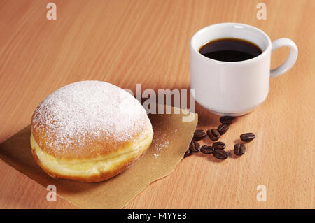 Tasse heißen Kaffee und Berliner Krapfen auf Schreibtisch Stockfoto