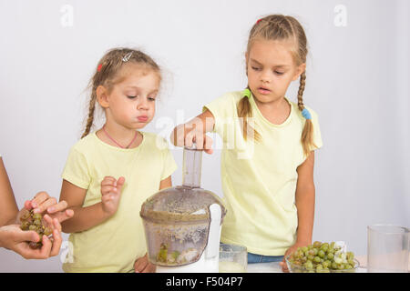 Zwei Mädchen an einem Tisch gepresster Saft von Birnen und Trauben mit einem Entsafter Stockfoto