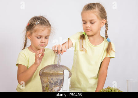 Zwei Mädchen an einem Tisch gepresster Saft von Birnen und Trauben mit einem Entsafter Stockfoto