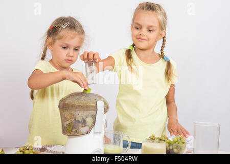 Zwei Mädchen an einem Tisch gepresster Saft von Birnen und Trauben mit einem Entsafter Stockfoto