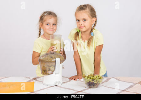 Zwei Mädchen an einem Tisch gepresster Saft von Birnen und Trauben mit einem Entsafter Stockfoto