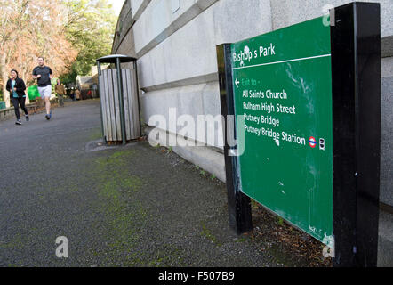 Wegweiser im Park des Bischofs, Fulham, London, England, mit Jogger im Hintergrund Stockfoto