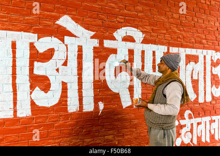 Mann Malerei weiße Buchstaben in Hindi Sprache an einer roten Wand Stockfoto