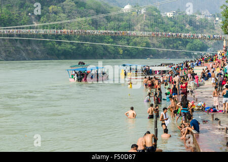 Pilger, die Badewanne am Ufer des heiligen Flusses Ganges, die Brücke Ram Jhula und eine Fähre in der Ferne Stockfoto