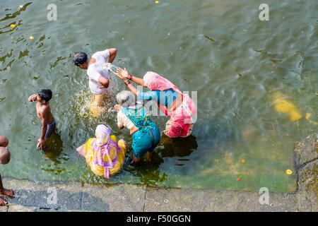 Drei Frauen spritzen Wasser bei einem Mann, stehend im heiligen Wasser des Flusses godwari Stockfoto