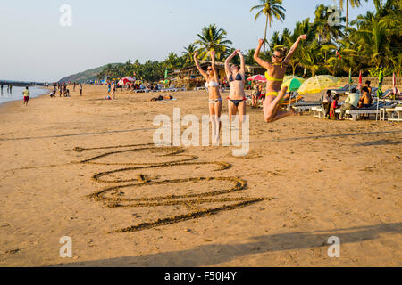 Drei junge Frauen Bikinis tragen, Springen nach dem Schreiben "Ich liebe Goa'im Sand von Anjuna Beach Stockfoto