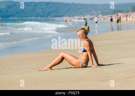 Eine junge Frau mit blondem Haar, tragen, Bikini, sitzt im Sand von Calangute Beach in der ehemaligen portugiesischen Kolonie Goa Stockfoto