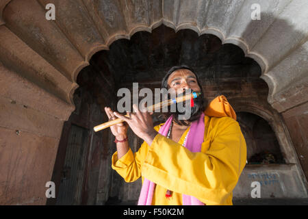 Ein Musiker in gelben Hemd spielt Flöte an der Ghats des Heiligen yamuna Fluss Stockfoto
