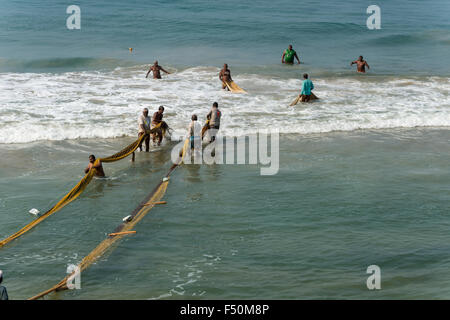 Eine Gruppe von Fischern, noch im Wasser stehend, zieht sich der Netze auf den Strand Stockfoto