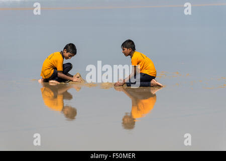 Zwei Schüler, tragen gelbe Hemden, Spielen mit Sand am Strand, die Spiegelung im Wasser Stockfoto