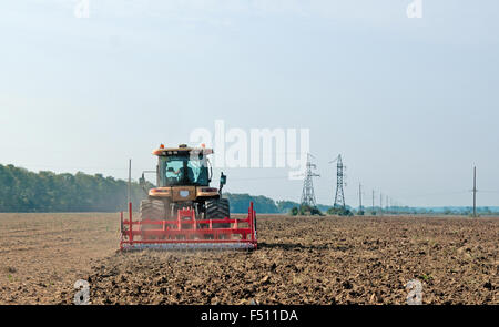 ein große gelbe Traktor verarbeitet das Feld Stockfoto