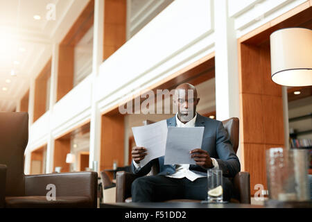 Porträt von beschäftigt junge Geschäftsmann sitzt in der Hotellobby Dokumente durchlaufen. Afrikanischen Geschäftsmann lesen Vertrag p Stockfoto