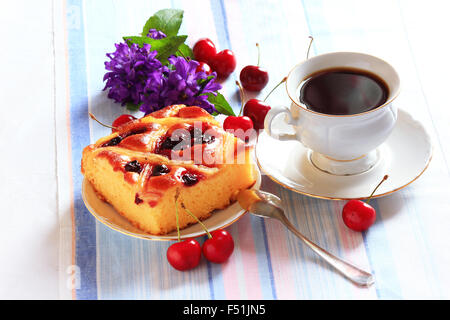 Stück Kirschkuchen auf einem Teller mit Cherriesand Teetasse im Hintergrund Stockfoto