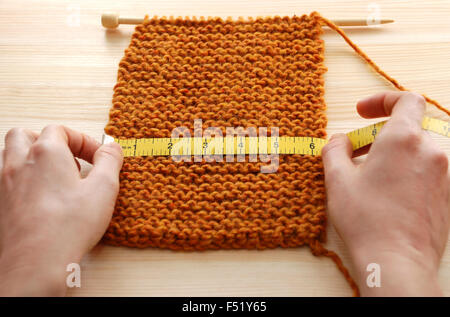 Zwei Hände halten ein Maßband über ein Stück stricken auf einem Holztisch, gemessen in Zoll Stockfoto