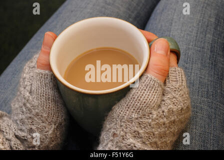 Eine Frau in einem warmen Pullover hält eine Tasse Tee oder Kaffee auf dem Schoß Stockfoto