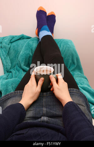 Frau hält eine Tasse Kaffee oder Tee, Entspannung auf der Couch mit ihren Füßen Stockfoto