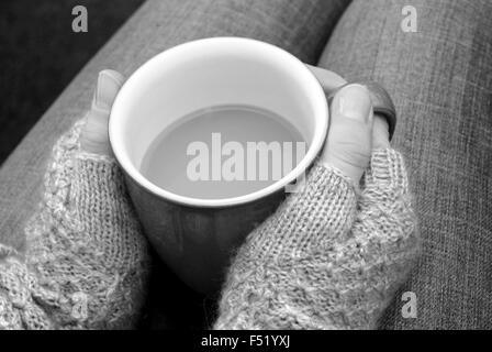 Eine Frau in einen warmen Pullover mit einer heißen Tasse Tee oder Kaffee auf dem Schoß - monochrome Verarbeitung Stockfoto