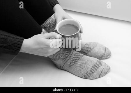 Frau mit einer Tasse Tee oder Kaffee, warme Winter Socken - monochrome Verarbeitung Stockfoto