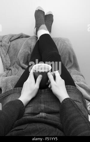 Frau hält eine Tasse Kaffee oder Tee, Entspannung auf der Couch mit ihren Füßen - monochrome Verarbeitungsgeschwindigkeit Stockfoto