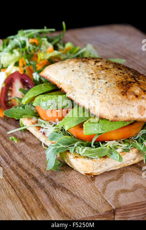 vegetarisches Sandwich mit Tomaten, Avocado und frischen Rucola serviert auf einem hölzernen Tay Stockfoto