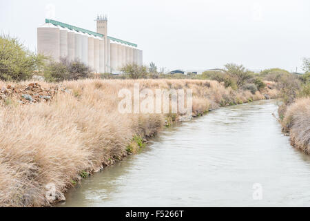 Einen Bewässerungskanal mit Getreidesilos in den Rücken bei Douglas, einer Kleinstadt in der Northern Cape Provinz von Südafrika Stockfoto