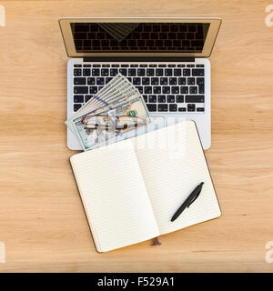 Laptop, Notebook mit einem Stift und Dollar Rechnungen auf einen leichten hölzernen Tischplatte Blick. Stockfoto