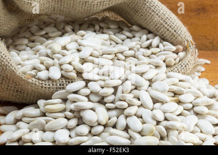 Natürliche weiße Bohnen in einem Beutel auf einem Holztisch Stockfoto