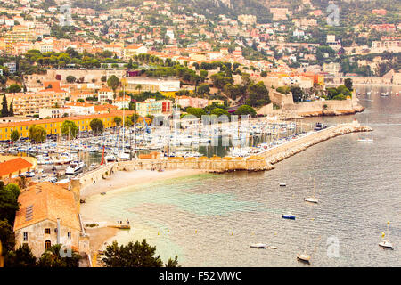 Ein erhöhter Blick auf eine Küstenstadt im mediterranen Stil mit einem geschäftigen Yachthafen voller Segelboote und Motoryachten. Ein Steinbruch erstreckt sich in das ruhige Meer und schützt den Hafen. Die Stadt Stockfoto
