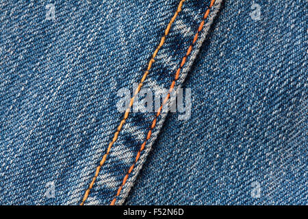 Detaillierte Nahaufnahme des blauen Denim-Materials mit strukturiertem Gewebe und diagonalem Twill-Muster. Eine Naht verläuft diagonal über das Bild, hervorgehoben durch hellorangefarbene Nähte, die einen Kontrast bilden Stockfoto
