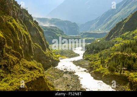 Ein breiter Fluss fließt durch ein tiefes Bergtal, flankiert von steilen, felsigen Hängen, die von üppiger grüner Vegetation bedeckt sind. Das Flussbett ist teilweise mit Felsen und Kies freigelegt, und das Wasser reflektiert sich Stockfoto