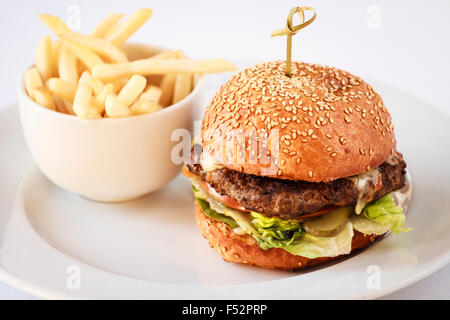 Beef-Burger in einem Sesam Brötchen mit einer Portion Pommes Frites auf einem weißen Teller Stockfoto