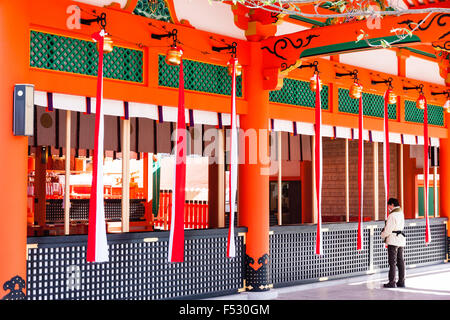 Kyoto Fushimi Inari Schrein. Blick entlang der Vorderseite des Heiligtums, Honden, große Halle mit Glocke Seile hängen. Mann, der betet durch tamagaki, Schutzzaun. Stockfoto